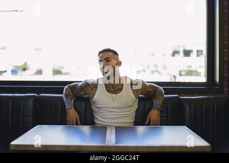 Jeune homme caucasien souriant avec des tatouages frais assis dans le café Banque D'Images