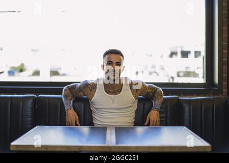 Jeune homme caucasien souriant avec des tatouages frais assis dans le café Banque D'Images