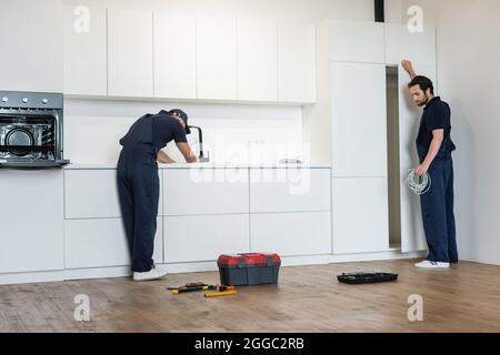 plombier et électricien travaillant dans une cuisine moderne près des outils sur le sol Banque D'Images