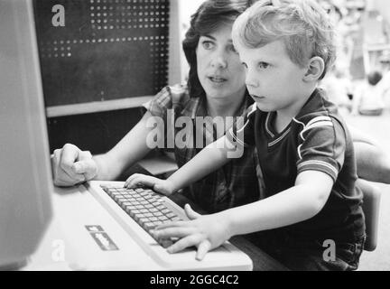 Austin Texas USA, circa 1989 : enseignant préscolaire travaille avec petit garçon sur ordinateur à la garderie. Bob Daemmrich Banque D'Images