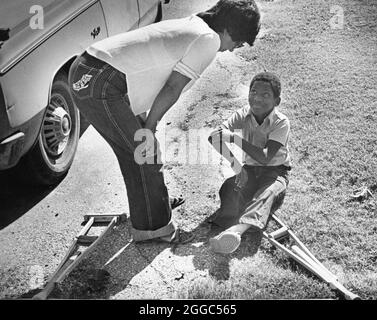 Austin, Texas USA, 1984 : Patrick Skeaton, garçon noir de quatrième année, qui a perdu sa jambe droite à cause du spina bifida, écoute sa mère assis sur le sol près de ses béquilles. Il a ensuite été équipé d'une prothèse de jambe. ©Bob Daemmrich Banque D'Images