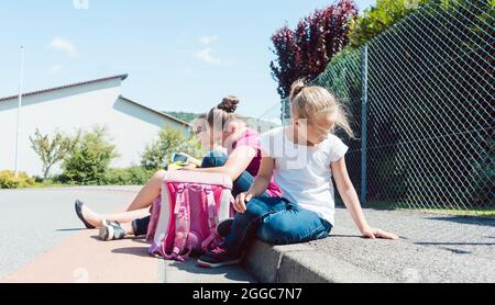 Trois filles en face de l'école attendant le bus Banque D'Images