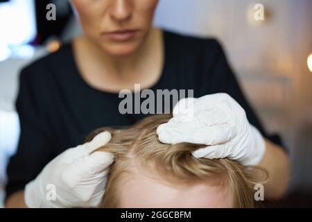 Gros plan sur la trichologue femme en gants de caoutchouc vérifiant les cheveux d'enfant. Banque D'Images