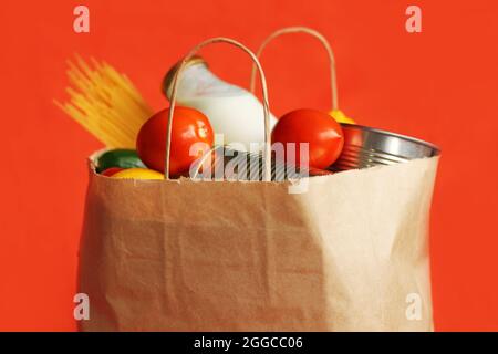 Produits dans un sac en papier sur fond rouge. Nourriture dans un service de livraison de nourriture. Aliments en conserve, pâtes, légumes, fruits, lait. Sans contact Banque D'Images