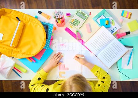 Retour à l'école. Vue supérieure d'une jeune fille moderne avec des livres de travail, papeterie, manuel et sac à dos ayant l'éducation à distance à la table blanche à la maison. Banque D'Images