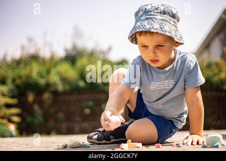 Joyeux petit garçon dessin hopscotch avec craie sur terre appréciant enfance heureuse à l'arrière-cour Banque D'Images