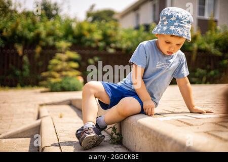 Joyeux petit garçon dessin hopscotch avec craie sur terre appréciant enfance heureuse à l'arrière-cour Banque D'Images