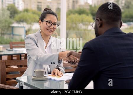 Une jeune femme d'affaires asiatique heureuse qui a pris la main d'un partenaire d'affaires africain après avoir négocié Banque D'Images