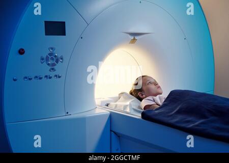 Petit patient sous une serviette bleue allongé sur une longue table de l'appareil d'IRM dans un laboratoire médical Banque D'Images