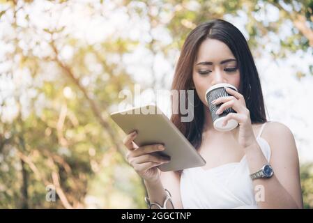 Woman Reading Online Article & Explore Online Feminist Website à partir d'une tablette et d'un café. Recherche Blog, contenu pour trouver la meilleure fiction littéraire Banque D'Images