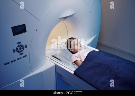 Petit patient des cliniques modernes va avoir un examen d'irm tout en étant couché sous une serviette bleue sur une longue table Banque D'Images