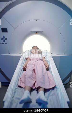 Petite fille allongé sur une longue table médicale et se déplaçant dans l'appareil d'irm dans les cliniques modernes Banque D'Images