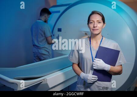 Jeune infirmière en uniforme et gants debout devant la machine médicale et son collègue Banque D'Images