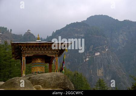 Grande roue de prière tibétaine 'mani' le long du sentier jusqu'au Paro Taktsang ou au monastère bouddhiste Tiger's Nest, avec le complexe du temple en arrière-plan, le Bhoutan Banque D'Images