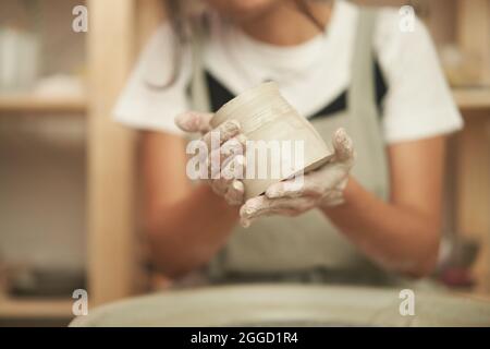 Récolte anonyme artisan tenant pot d'argile humide dans les mains sales après le processus de moulage sur la roue de poterie pendant le travail en studio professionnel Banque D'Images