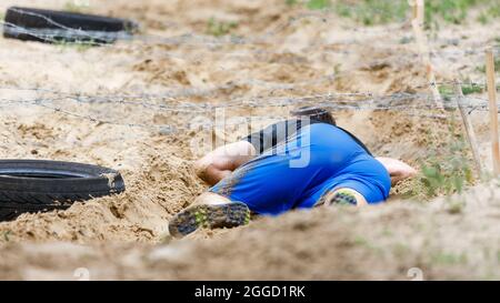 Sportsman rampant sous un obstacle barbelé sur son parcours en course d'obstacle Banque D'Images