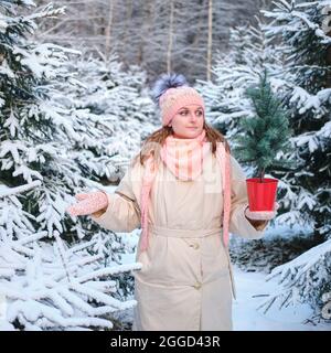 Une femme choisit un arbre de Noël artificiel ou naturel dans la pépinière en nature d'hiver à la Saint-Sylvestre Banque D'Images