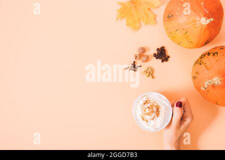 Femme tenant main une tasse de latte d'épices de citrouille à côté des tas de assaisonnements et de citrouilles Hokkaido bio entières sur fond orange avec espace de copie Banque D'Images