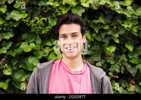 portrait d'un jeune homme heureux souriant regardant l'appareil photo sur un fond de plantes vertes, concept des expressions humaines et des émotions, copier l'espace pour le texte Banque D'Images