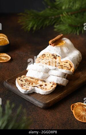 Traditionnel stollen décoré de tranches d'orange sur un fond marron avec des branches à feuilles persistantes. Vacances de Noël cuisine traditionnelle. Gros plan. Banque D'Images