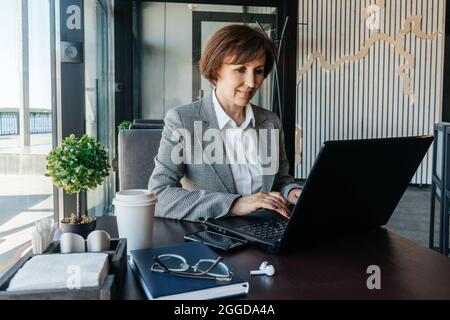 Femme d'affaires senior dans un blazer blanc travaille dans un café. Travail à distance. Banque D'Images