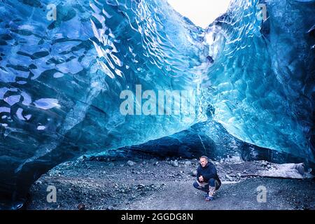 À l'intérieur d'une grotte de glace glaciaire bleue dans le glacier. Breioarmerkurjokull, une partie du glacier Vatnajokull, dans le sud-est de l'Islande. Un homme se croupe à l'en Banque D'Images