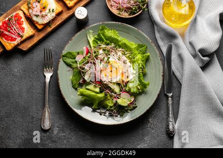 Assiette de salade savoureuse avec légumes, œuf frit et micro-vert sur fond sombre Banque D'Images