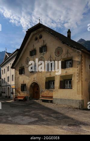 La façade colorée peinte et décorée de cette ancienne maison familiale, restaurée en 1946, contraste avec le design néoclassique austère et tourniqué de l'édifice qui l'a dépassé à Scuol Sot, la vieille ville au-dessus de l'auberge de la rivière alpine ou à Scuol, Grisons ou Grisons canton, Suisse. Beaucoup des maisons traditionnelles ici ont été rénovées beaucoup plus récemment, avec de nouveaux propriétaires qui s'occupent de préserver des caractéristiques historiques telles que des fours à pain, des armoiries peintes et des inscriptions. Banque D'Images