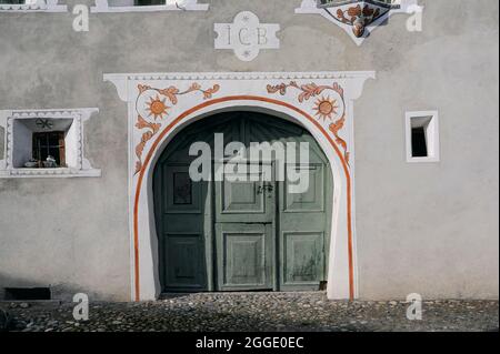 La décoration sgraffito blanche avec des détails peints en orange complète le bois lambrissé vert clair, centré sur une porte stable, remplissant l'entrée ronde de cette maison familiale restaurée à Scuol Sot, la vieille ville construite à proximité de la rivière alpine Inn ou à Scuol, Canton des Grisons ou Grisons, Suisse. Banque D'Images