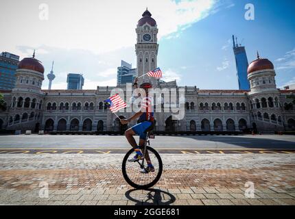 Kuala Lumpur, Malaisie. 31 août 2021. Un homme passe un monocycle tout en tenant des drapeaux malaisiens lors des célébrations de la 64e Journée nationale à Kuala Lumpur.la Malaisie célébrant chaque année son 64ème jour de l'indépendance le 31 août, elle commémore la Déclaration d'indépendance de Malaisie du 31 août 1957. Crédit : SOPA Images Limited/Alamy Live News Banque D'Images