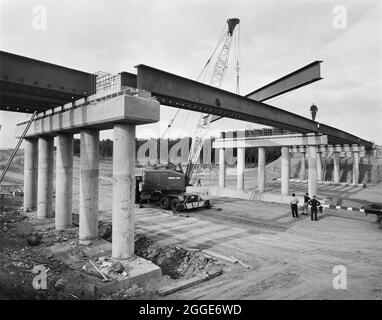 Vue sur la construction de l'autoroute Midland Link, entre la sortie 13 et la sortie 11 de la M6, montrant des poutres d'acier en cours d'abaissement sur l'un des ponts. Cette photographie a été publiée en octobre 1964 dans la lettre d'information mensuelle de Laing 'Team Spirit'. Banque D'Images