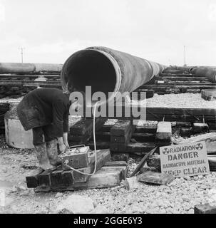 Un travailleur qui réalise une radiographie du pipeline North Coates, en vérifiant les défauts de soudage. Les travaux de génie civil sur le pipeline de North Coates ont été réalisés par Laing pipelines ainsi que par les sociétés françaises Entrempose et GTM. Plus de deux miles de pipeline de 36 pouces de diamètre, enfermé dans du béton, a été ensuite tiré en mer dans l'estuaire du Humber. Banque D'Images