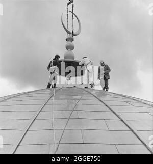 Mosquée centrale de Londres et centre culturel islamique, Park Road, Regent's Park, Cité de Westminster, Autorité du Grand Londres, 15/03/1977. Des hommes portant des harnais de sécurité positionnant le croissant sur le toit bombé de la salle de prière de la mosquée centrale de Londres, comme il est abaissé par une grue. Le fiel a été fabriqué à partir de béton armé en fibre de verre (GRC) dans le Northamptonshire, et peint dans le sud du pays de Galles pour donner une finition dorée. Banque D'Images