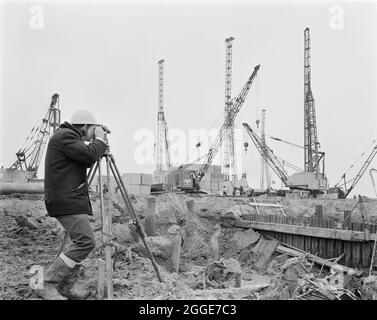 Un arpenteur de Laing utilisant une théodolite sur le chantier de construction de la centrale de l'île de grain. La centrale de l'île de grain était une centrale au mazout construite dans les 1970&#x2019;s par plusieurs entrepreneurs, dont John Laing et son Ltd. Lorsque la centrale a ouvert en 1979, elle avait la deuxième cheminée la plus haute au Royaume-Uni à 244 mètres de haut. La centrale a été démolie et la cheminée a été détruite en septembre 2016. Une nouvelle centrale à turbine à gaz à cycle combiné (CCGT) a été construite sur le site. Banque D'Images