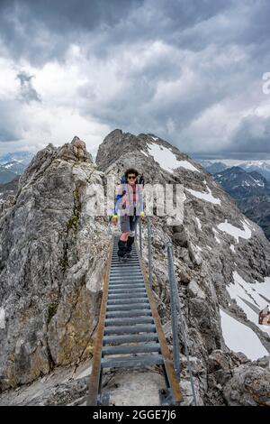 Randonneur sur un pont métallique sur une roche, sentier de crête avec des restes de neige, panorama de montagne avec haute lumière de pic, ciel nuageux spectaculaire, Heilbronner Weg Banque D'Images