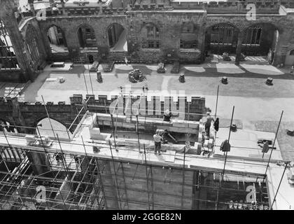 Une vue des constructeurs travaillant au sommet de l'échafaudage sur la construction de la cathédrale de Coventry, avec les ruines de l'ancienne cathédrale derrière. La photo montre la construction de la nouvelle cathédrale de Coventry, conçue par Basil Spence en 1951 et construite entre le milieu des années 1950 et 1962. Il a remplacé l'église de la cathédrale Saint-Michel en ruines qui avait été gravement endommagée par les bombardements en 1941. Banque D'Images