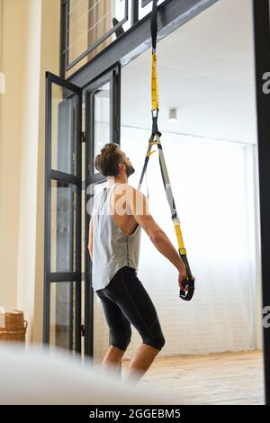 Jeune homme sportif utilisant un bracelet de résistance pendant l'entraînement à la maison Banque D'Images