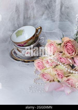 Shabby chic mariage encore vie arrangement avec des fleurs roses, des tasses de thé vintage et des perles. Banque D'Images