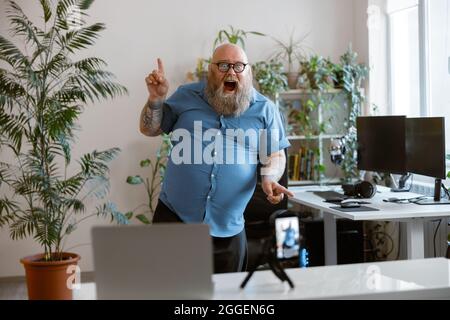 Drôle barbu homme obèse danse enregistrement de nouvelles vidéos pour le blog avec téléphone à la maison Banque D'Images