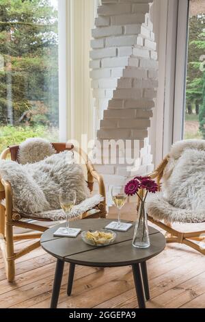 Deux chaises en osier avec oreillers et table basse avec verres à vin et en-cas dans un jardin d'hiver, vertical Banque D'Images