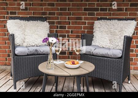 Deux chaises en rotin avec coussins et une petite table avec verres à vin sur une terrasse en bois, mur en pierre en arrière-plan Banque D'Images