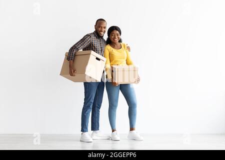 Portrait complet de Happy Black couple debout avec des boîtes en carton dans les mains dans leur nouvel appartement, joyeux conjoints afro-américains portant Bel Banque D'Images