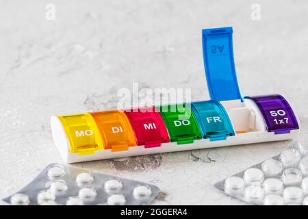 Boîte de pilules colorées pour le dosage hebdomadaire sur fond blanc, abréviations pour les jours de la semaine en allemand Banque D'Images