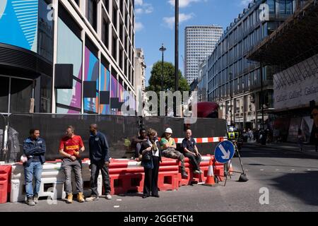 Ouvriers assis dans une file d'attente prenant une pause dans un chantier de construction le long d'Oxford Street le 10 août 2021 à Londres, Royaume-Uni. Banque D'Images