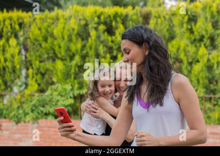 Deux jeunes femmes et une petite fille prennent des selfies et s'amusent dans le jardin de leur maison. Femme sélective Banque D'Images