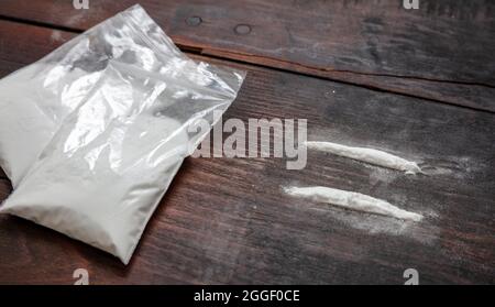 Paquets de plastique de cocaïne et deux lignes. Drogues stupéfiants addiction concept. Poudre blanche sur fond de table en bois, gros plan. Banque D'Images