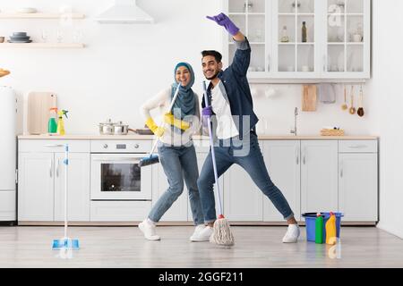 Beau heureux jeune couple musulman nettoyer le sol et s'amuser dans la cuisine ensemble, pleine photo, copier l'espace. Drôle de dame dans hijab et son chanter Banque D'Images