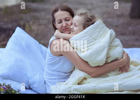 Une femme épouse l'enfant lorsqu'elle est assise sur le lit. L'enfant est couvert d'une couverture à l'extérieur. Banque D'Images
