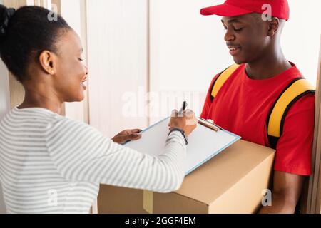 Service de livraison. African American Woman Signing Papers recevoir carton boîte colis de Courier debout à la maison. Concept d'expédition de colis. Sélectionnez Banque D'Images