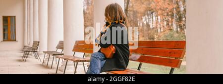 c'est l'automne. belle femme voyageur habillée à l'automne. la jeune fille est assise sur un banc et regarde l'architecture du bâtiment dans le parc. Banque D'Images